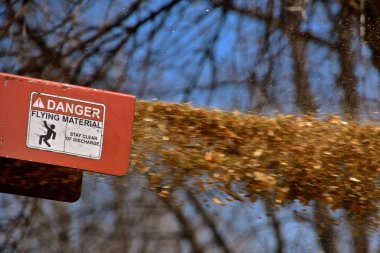 A wood shredder blows refuse into a trailer at a high speed where a sign reads DANGER of FLYING MATERIAL clipart