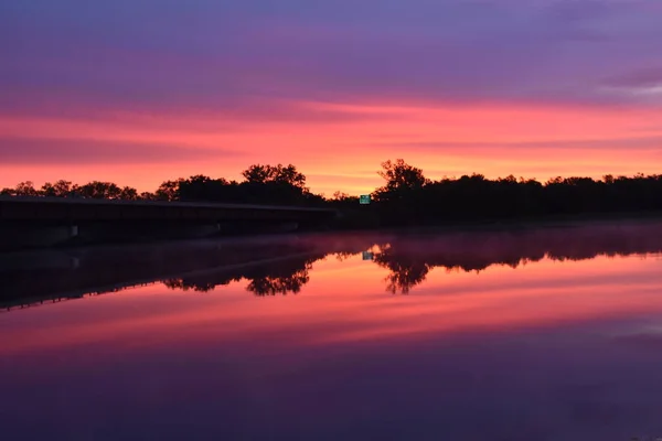 日出使密西西比河上一片红色 隐约看到一座桥和一个绿色的路标 — 图库照片
