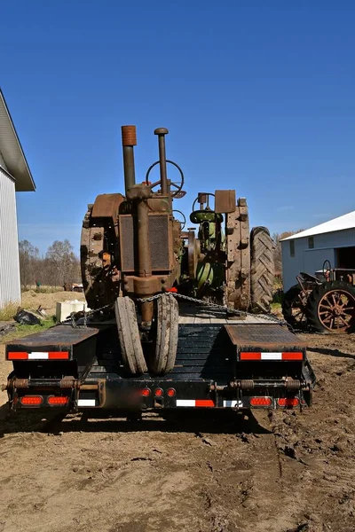 An old tractor with lugs on the wheels is secured to a flat bed trailer for transport.