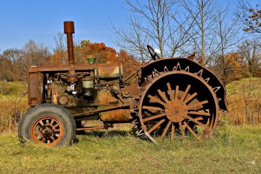  An old unidentifiable rusty tractor with lug wheels is left isolated in a woods