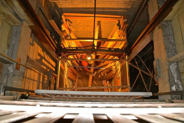 Old functional elevator and shaft in a warehouse used to transfer freight with light bulb illumination.