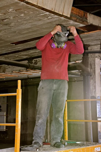 一名身份不明的工人在一家旧仓库的整修工程中戴上防尘面罩 — 图库照片