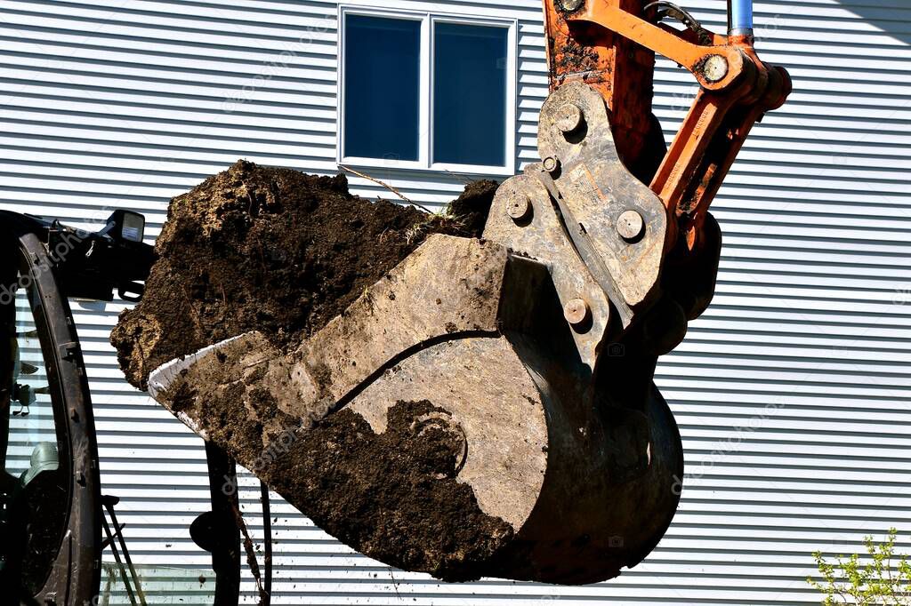 An excavating bucket filled with earth is being moved from a construction site. 