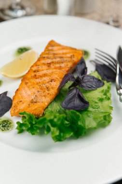 Salata yaprakları ve beyaz plaka üzerinde limon ile balık