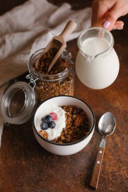 Kahvaltı için taze turuncu granola. Granola kase süt dökülen kadın