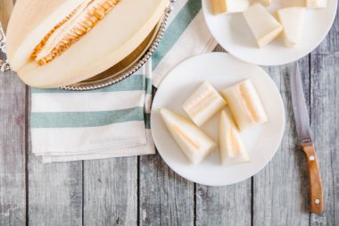 Yukarıdan kesilerek kavun metalik çanak ve bıçak ve çizgili peçete ile beyaz tabaklar