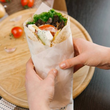 Kısmi tutan kadın görünümünü shawarma parşömen kağıt arka plan bulanık üzerine sarılı ızgara