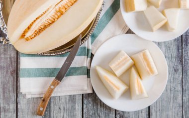 Dilimlenmiş kavun üstten görünüm metalik çanak ve bıçak ve çizgili peçete ile beyaz tabaklar