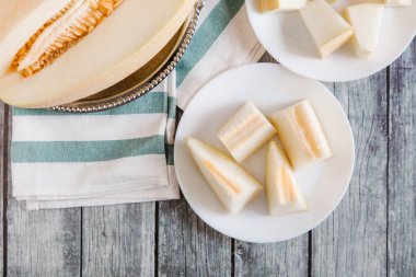 Yukarıdan kesilerek kavun metalik çanak ve bıçak ve çizgili peçete ile beyaz tabaklar