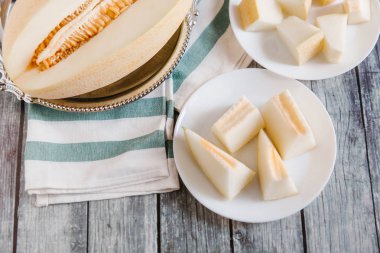 Yukarıdan kesilerek kavun metalik çanak ve bıçak ve çizgili peçete ile beyaz tabaklar