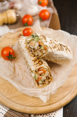 Gevrek ve sulu shawarma parşömen kağıt ve yuvarlak ahşap plaka üzerinde domates ile servis