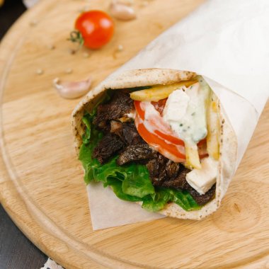 Parşömen kağıt arka plan bulanık üzerine sarılı ızgara shawarma ile ahşap plaka