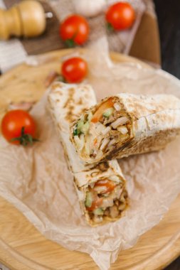 Gevrek ve sulu shawarma parşömen kağıt ve yuvarlak ahşap plaka üzerinde domates ile servis