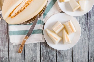 Dilimlenmiş kavun üstten görünüm metalik çanak ve bıçak ve çizgili peçete ile beyaz tabaklar