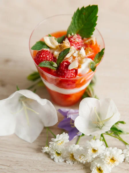 Strawberry yogurt with mint, whole strawberries and cashew on top, on wooden surface and flowers around