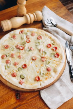 Keten peçete ve çatal bıçak ile ahşap trencher üzerinde lezzetli Pizza salam ve salatalık ile yüksek açılı görünüş