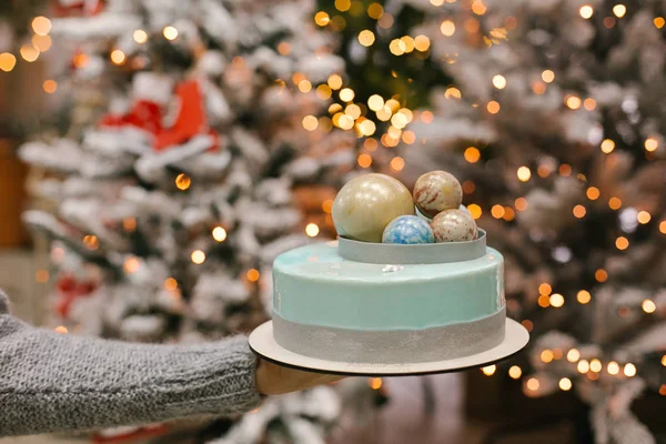 Close view of Christmas cake with chocolate balls on top on female hand with blurred lights on background