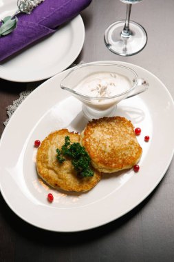 Ekşi krema ve maydanoz ile beyaz tabakta servis Draniki