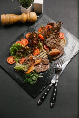 Izgara sığır eti taze sebze ve salata ile servis kara tahta üzerinde yapraklar