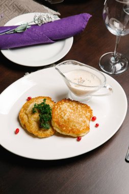 Ekşi krema, maydanoz ve menekşe peçete ile beyaz tabakta servis Draniki