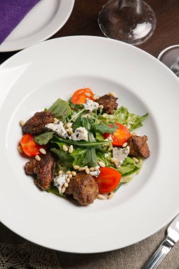 Beyaz tabakta salata sığır eti, domates, roka, çam fıstığı ve dor blu closeup görünümünü