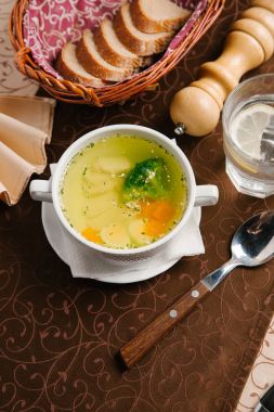 Tavuk çorbası yumurta yarısı, brokoli, tavuk ve havuç dilimleri parçası ile beyaz kase kaşık ile hizmet.