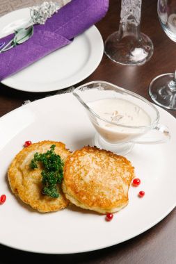 Ekşi krema ve maydanoz ile beyaz tabakta servis Draniki