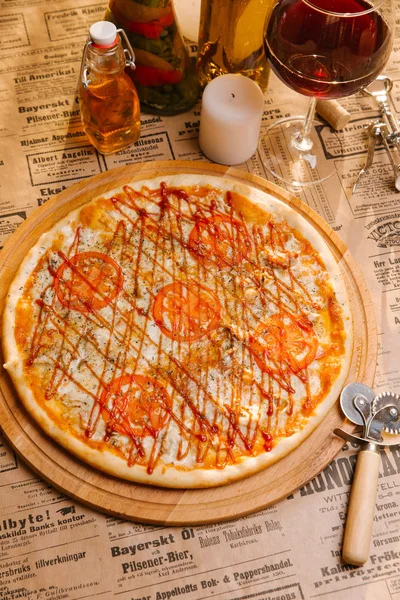 Chicken pizza with mozzarella, tomatoes and ketchup on top served on wooden board