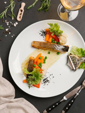 Bebek havuç, yeşil yaprakları ve limon dilimi ile kavrulmuş beyaz balık biftek servis