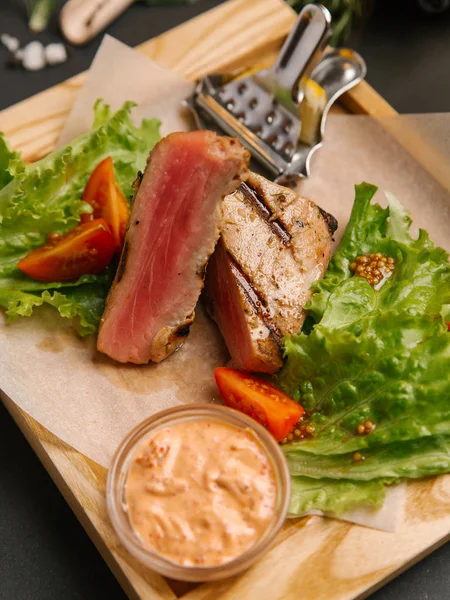 Dilimlenmiş yeşil yaprakları, hardal ahşap tepsi ve domates ile servis kaburga eti