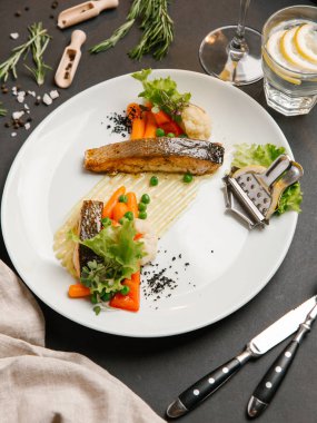 Bebek havuç, yeşil yaprakları ve limon dilimi ile kavrulmuş beyaz balık biftek servis