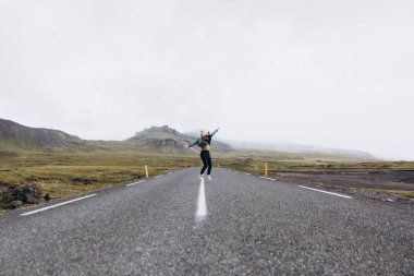Genç kadın yolda soğuk yağmurlu günde Dağları arka plan atlama yan görünüm