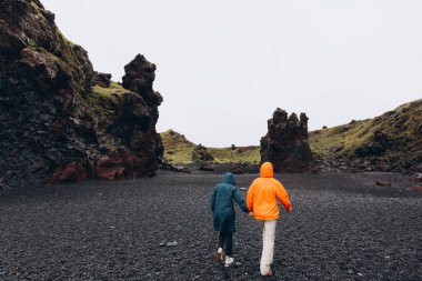Kıyı dışında soğuk yağmurlu günde yürüyüş trençkotlar giyen genç çiftin arkadan görünüş