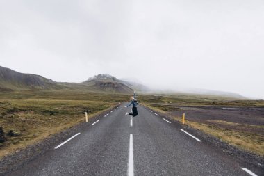 Genç kadın yolda soğuk yağmurlu günde Dağları arka plan atlama yan görünüm