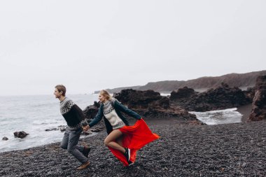 Yağmurlu günde kayalık sahilin yanında çalışan genç Çift