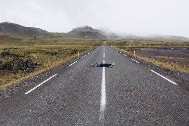 Genç kadın soğuk yağmurlu günde Dağları arka plan üstünde belgili tanımlık yol döşeme yan görünüm