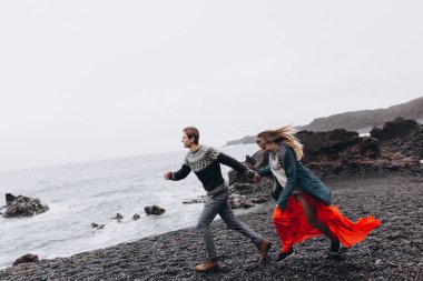 Yağmurlu günde kayalık sahilin yanında çalışan genç Çift