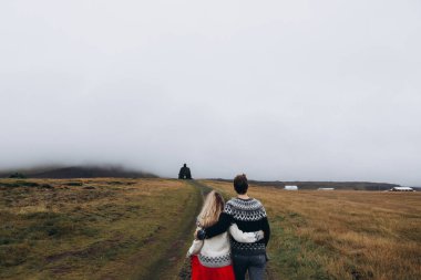 Çayır on sarılma örme kazak giyen genç çiftin arkadan görünüş