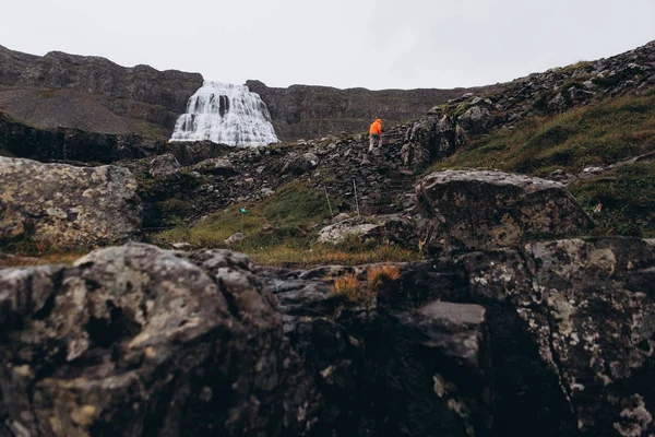 View of man walking by mountain path to see waterfall in cold rainy day