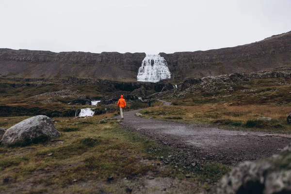 View of man walking by mountain path to see waterfall in cold rainy day