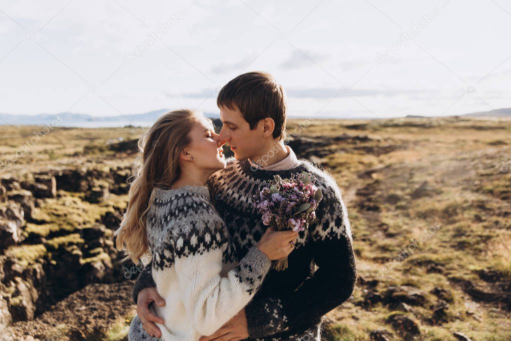 Young couple dressed in knitted sweaters kissing on peak of mountain