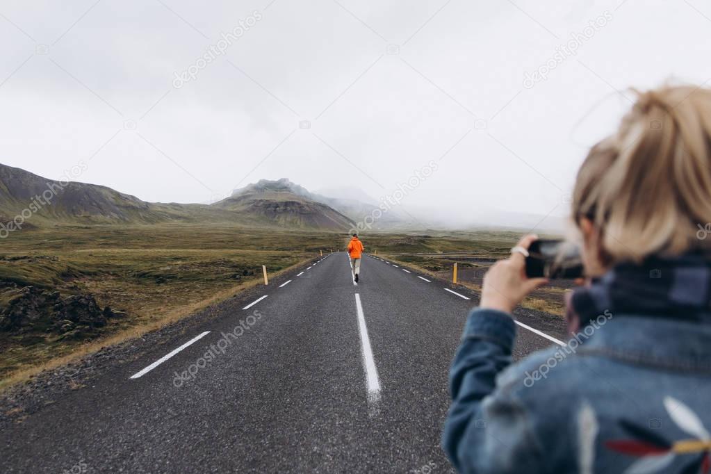 Young woman with smartphone taking video of man running by road