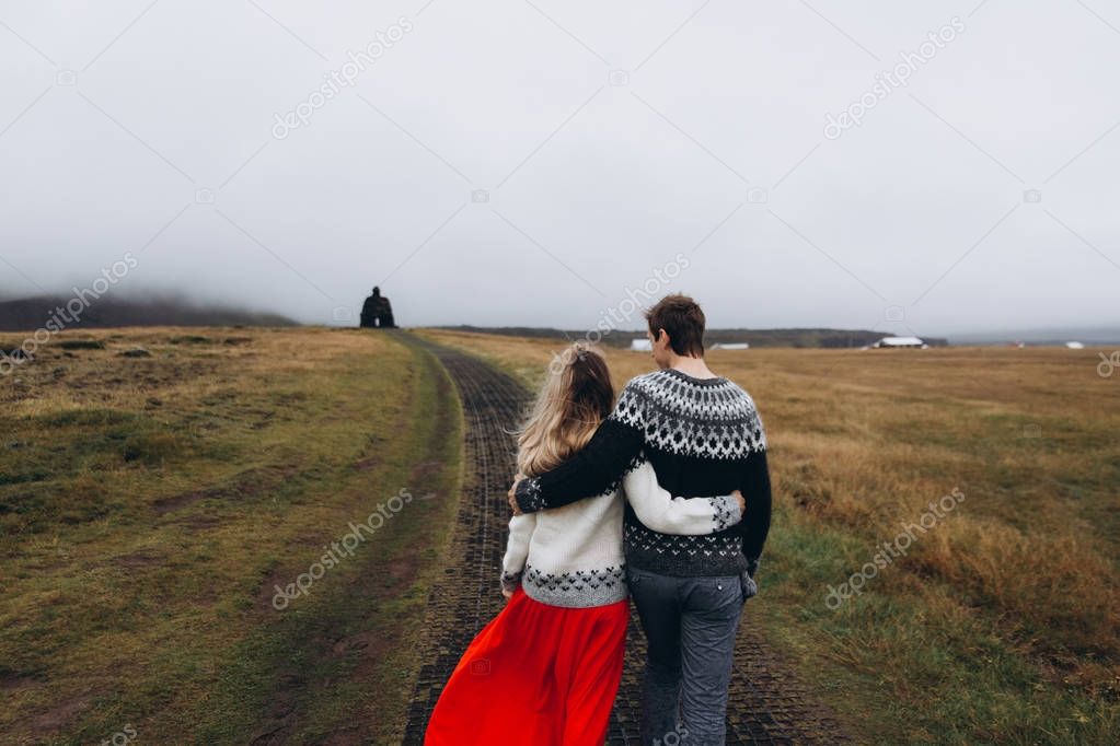 Rear view of young couple wearing knitted sweaters hugging on meadow