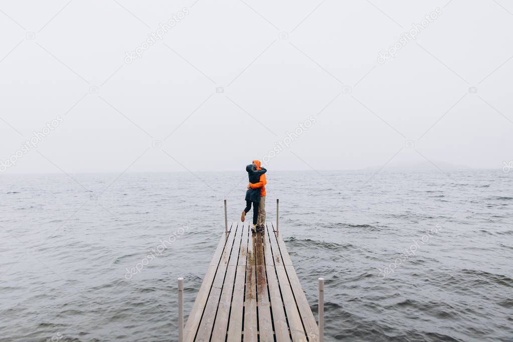 Young couple hugging and standing on pier in rainy day