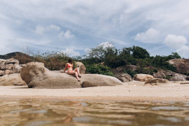 Kayalar oturan ve çiçek arka plan üzerinde poz kırmızı bikini giyen kadın görünümünü.