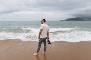 Sahilde yürüyüş ve sandalet elinde tutan şık adam yan görünüm