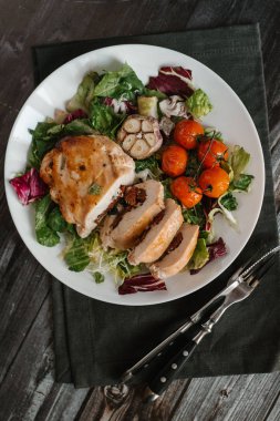 Kurutulmuş domates karışık salata yaprakları üzerinde pişmiş domates ve sarımsak kafa ile servis ile iştah açıcı yemek kompozisyon pişmiş tavuk fileto ile doldurulmuş