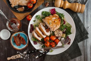 Pişmiş domates ve sarımsak kafası karışık salata yaprakları üzerinde hizmet güneş kurutulmuş domates ile doldurulmuş ve dilimlenmiş, fırında tavuk fileto görünümünü kapat