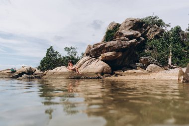 Doğal kayalık zemin üzerine poz kırmızı bikini giyen kadın yan görünüm.