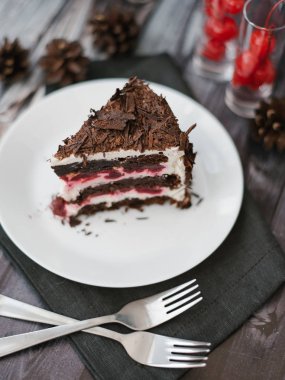 Görünüm kiraz ve yoğurt dolum ile çikolatalı kek parçasının servis beyaz tabak çatal ile koyu ahşap masa arka plan üzerinde peçete ve çam kozalakları